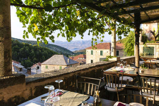 Terrasse mit Tischen und Stühlen mit schöner Aussicht auf die Stadt Dol, das Meer und die Berge