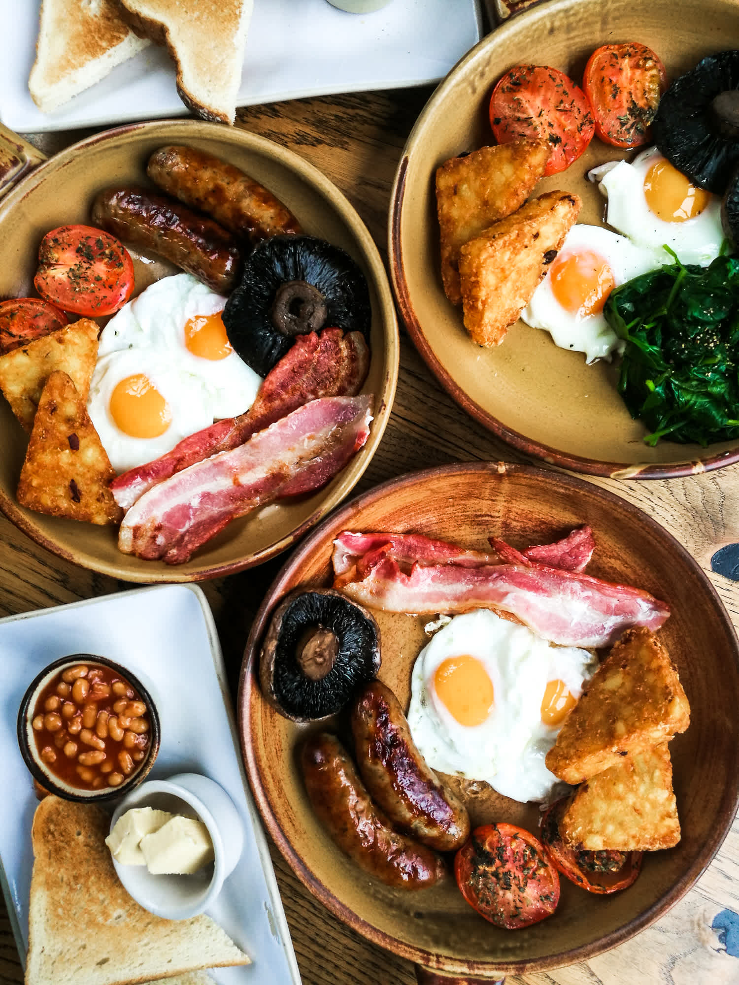Plusieurs assiettes avec au menu le fameux English Breakfast, grande spécialité du petit-déjeuner anglais à déguster pendant votre séjour en Angleterre.