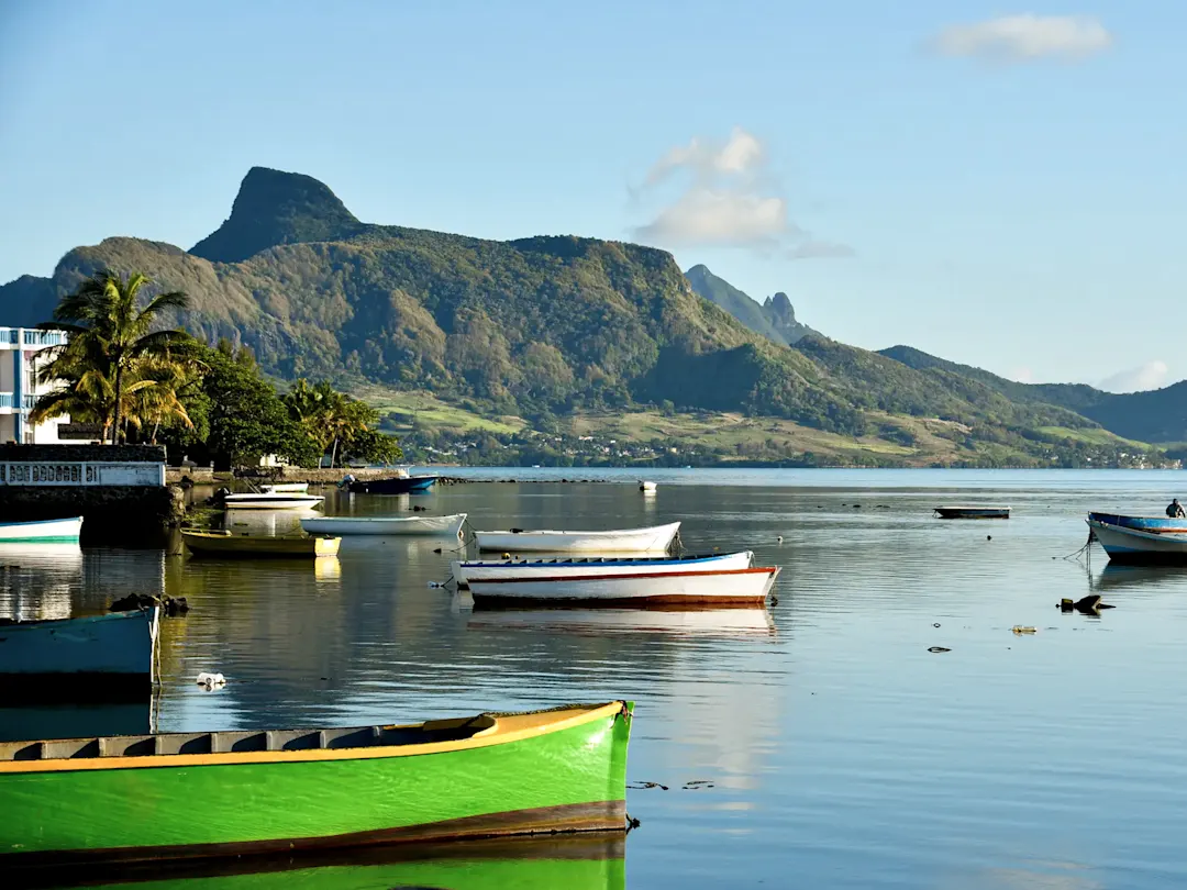 Bunte Boote auf ruhigem Wasser mit üppigen Bergen im Hintergrund. Mauritius.