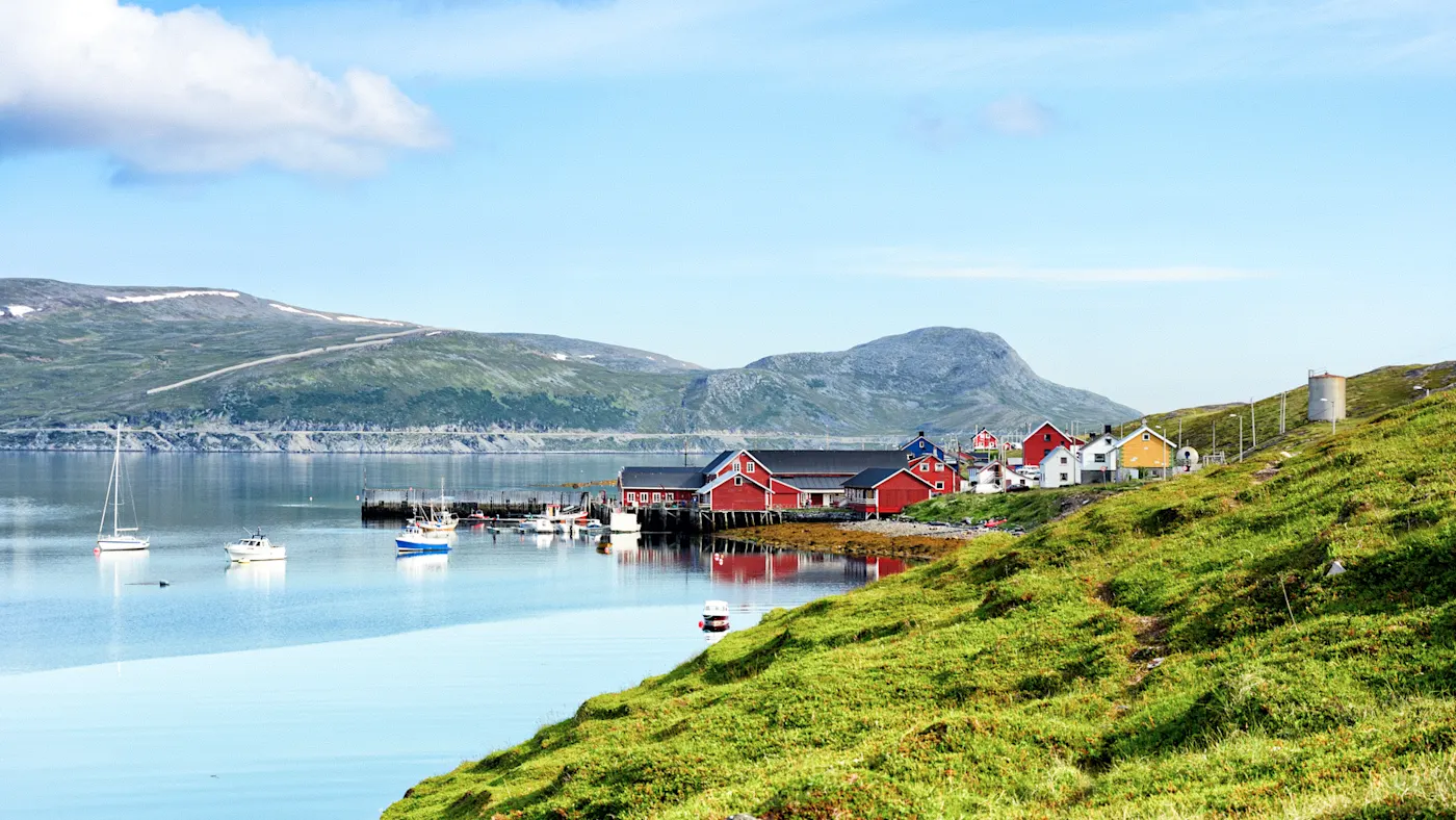 Kleines Fischerdorf mit roten und gelben Häusern am Ufer eines Fjords, Nordkap, Norwegen.