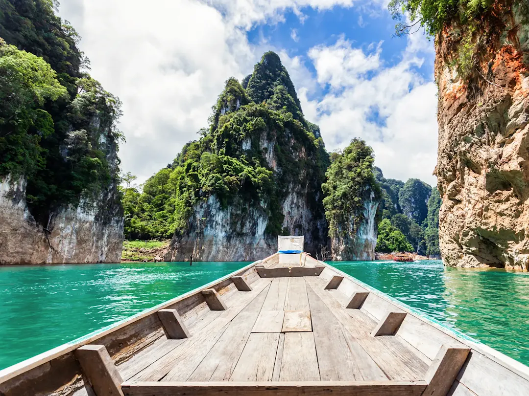 Holzboot auf türkisfarbenem Wasser mit Kalksteinfelsen. Khao Sok, Thailand.