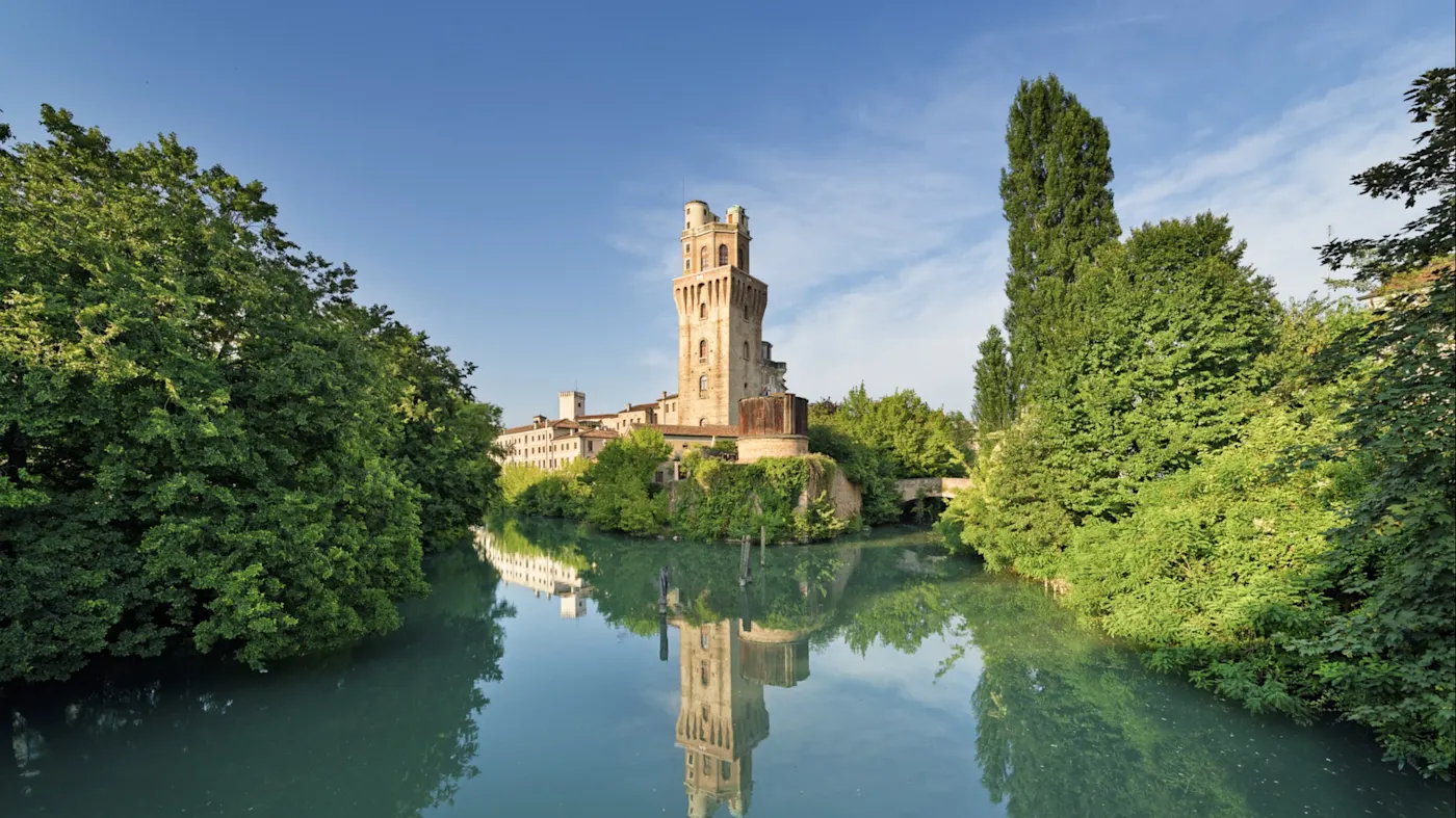 Reflektion des mittelalterlichen Turms und grüner Bäume in einem ruhigen Kanal, Padua, Venetien, Italien.
