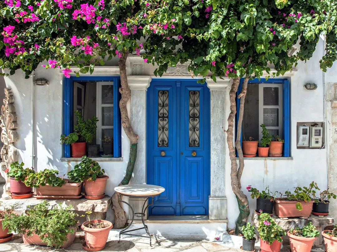 Blaue Türen und Fenster mit Blumen geschmücktem Eingangsbereich. Insel Paros, Kykladen, Griechenland.