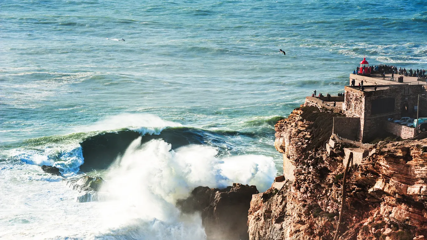 Nazaré, Leiria, Portugal Große Wellen schlagen gegen die Klippen unter dem Leuchtturm von Nazaré, Nazaré, Leiria, Portugal.