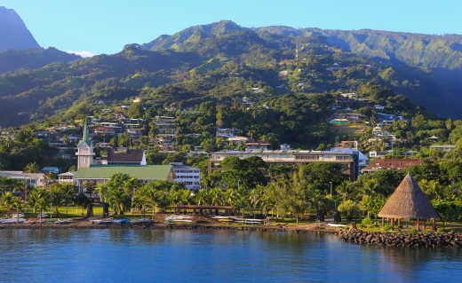 South Pacific Islands, French Polynesia, Papeete skyline seen from offshore, green mountains rise in the background.