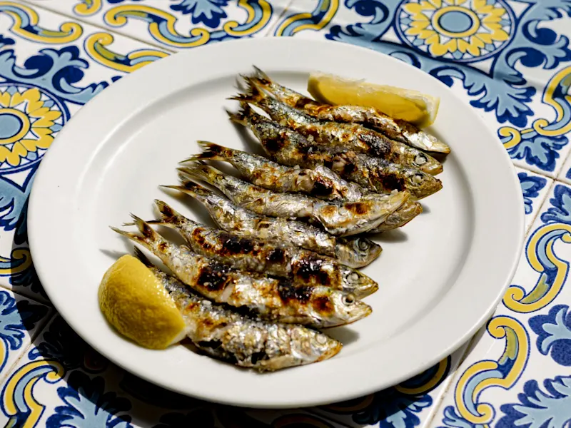 Gegrillte Sardinen auf einem weißen Teller mit Zitronenspalten, serviert auf einem dekorativen Tisch. Málaga, Andalusien, Spanien.