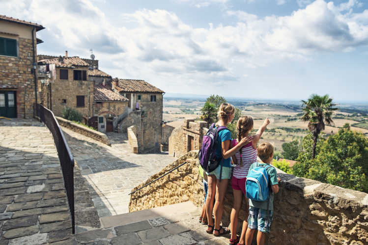 Eine Mutter und drei Kinder in einem Dörfchen in der Toskana als Sinnbild für einen Familienurlaub in Italien