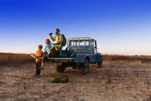 Vater, Mutter und Sohn mit Jeep in der Wildnis beim Familienurlaub in Kenia