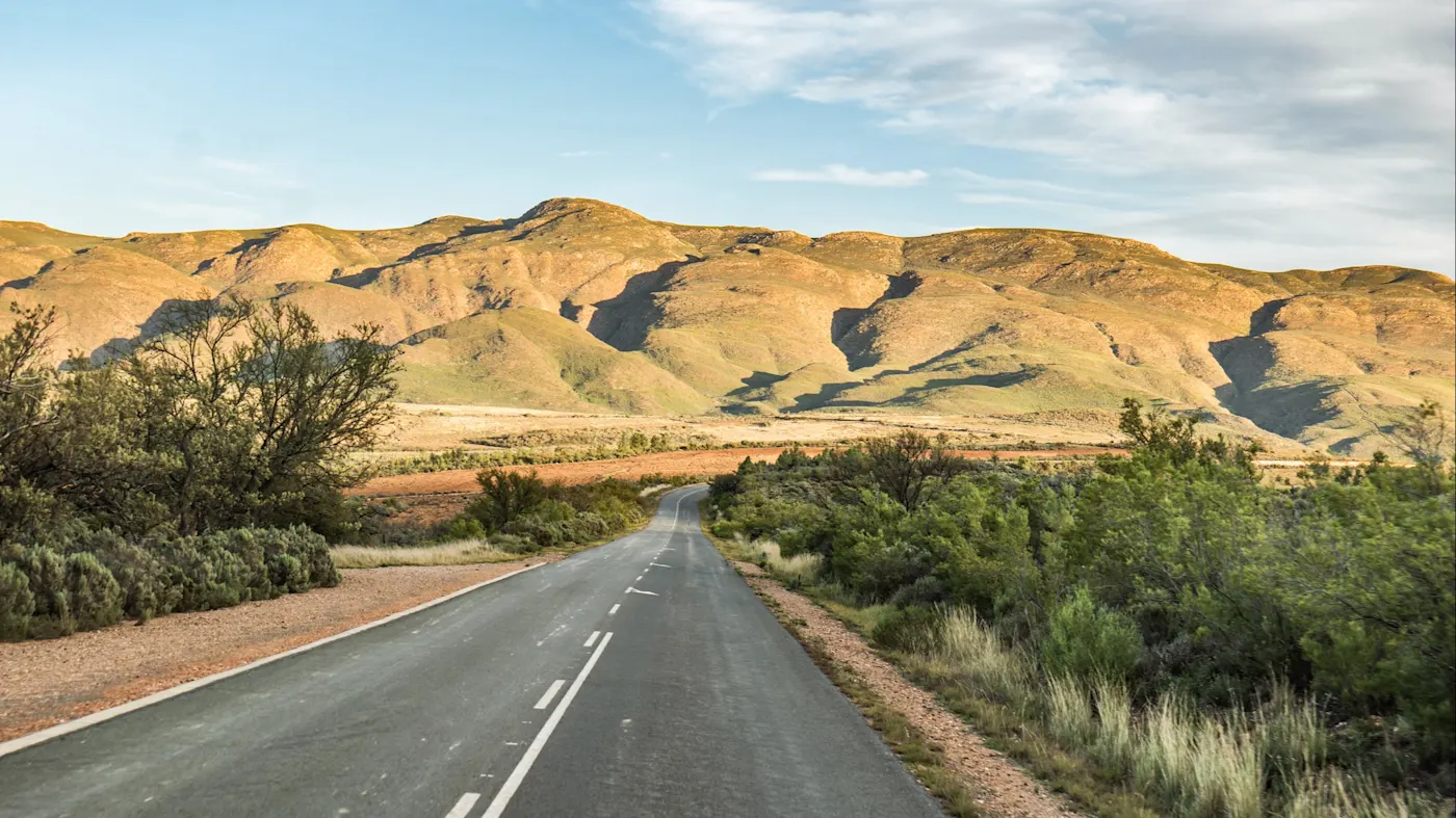 Oudtshoorn, Westkap, Südafrika Endlose Straße durch eine karge Hügellandschaft in der Abendsonne. Oudtshoorn, Westkap, Südafrika.