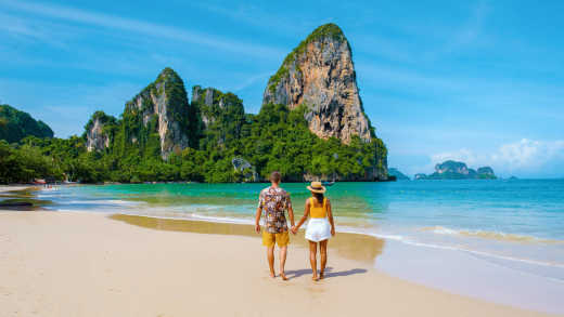 Ein Paar, das Händchen hält, steht an einem tropischen Strand in Thailand und genießt seine Flitterwochen