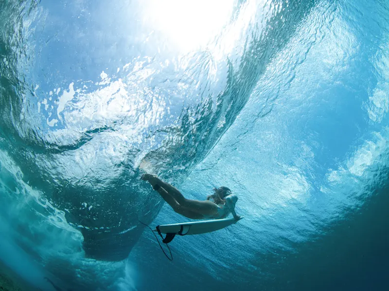 Unterwasseraufnahme eines Surfers, der unter einer brechenden Welle paddelt. Französisch-Polynesien.