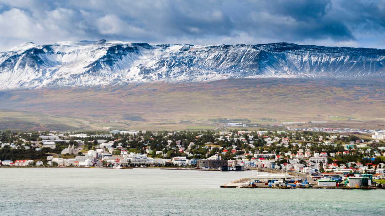 Europe, Iceland, Akureyri seen from offshore with snowy mountains in the background.