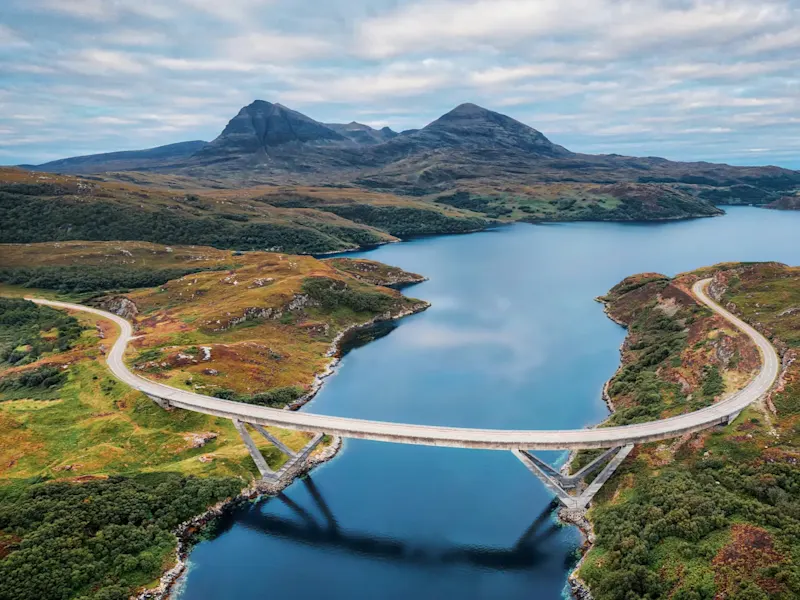 Scotland, Kylesku-Brücke, Road Trip Kylesku-Brücke, die über ein Gewässer verläuft, mit grünen Hügeln und Bergen im Hintergrund. Schottland.