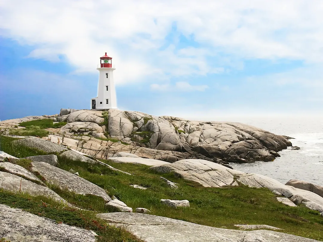 Weißer Leuchtturm auf felsiger Küste mit blauem Himmel. Peggy’s Cove, Nova Scotia, Kanada.
