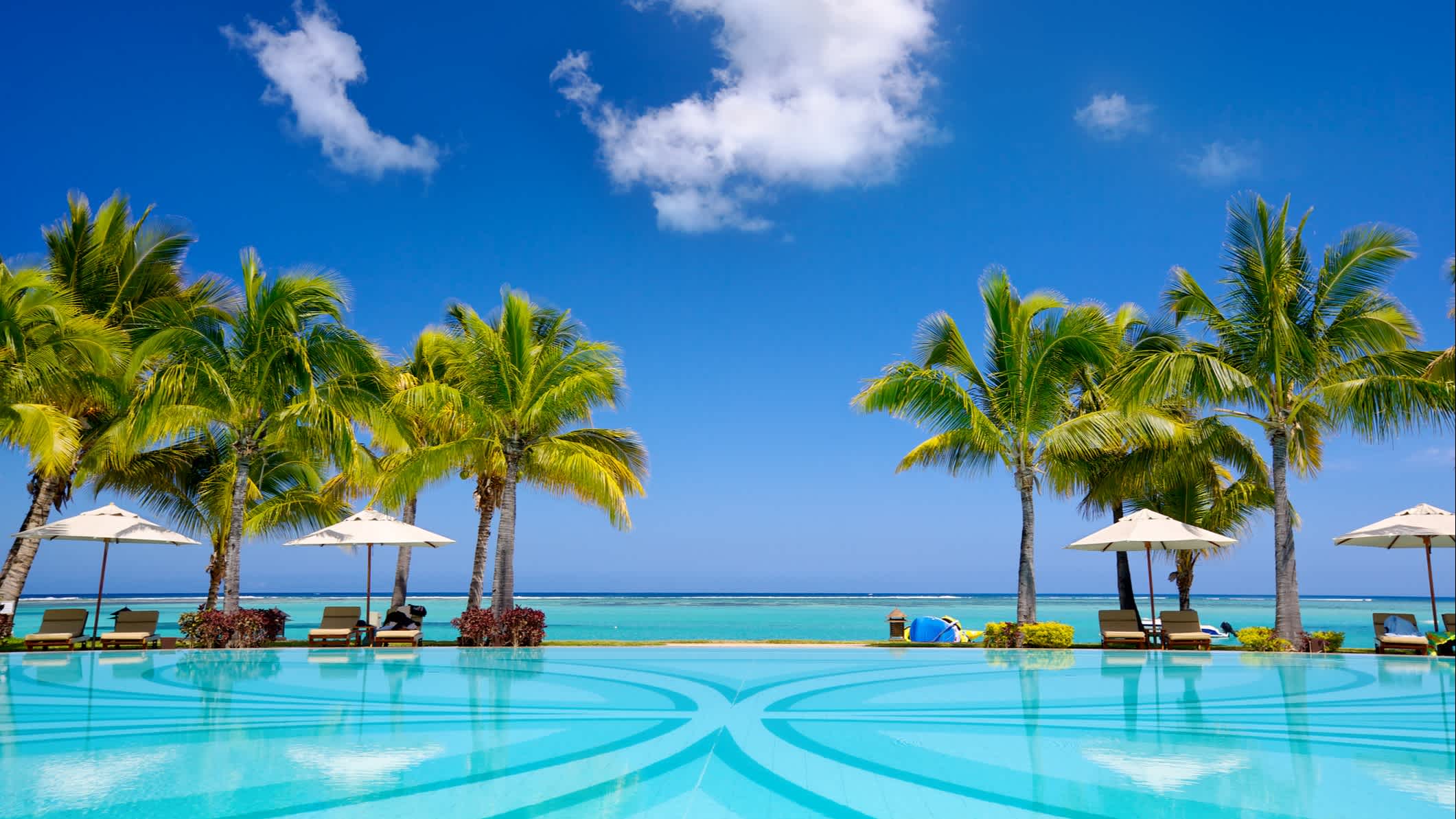 Chaises longues et parasols au bord d'une piscine avec la mer en arrière-plan à l'île Maurice
