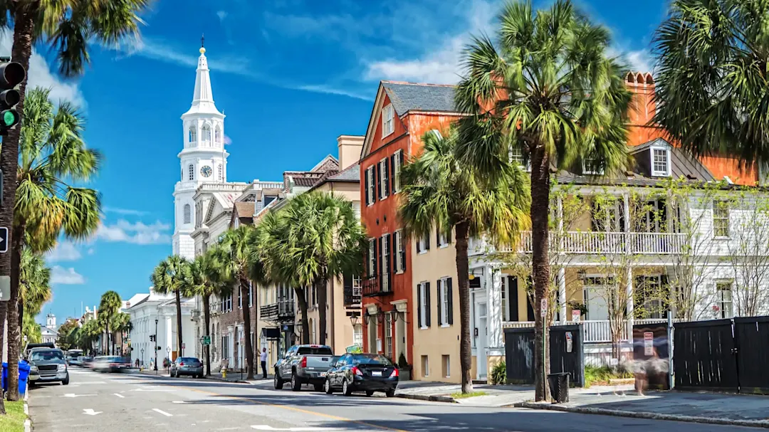 Historische Straße mit Palmen und Kirchturm unter blauem Himmel. Charleston, South Carolina, USA.