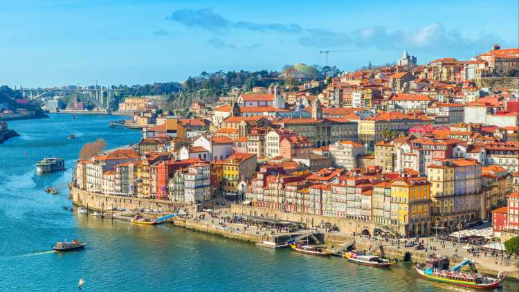 Europe, Portugal, Porto, the Porto skyline seen from 
Douro River. Blue sky and brightly lit buildings with red tile roofs.