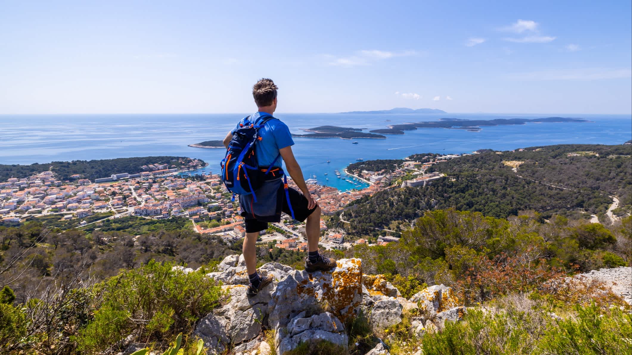 Mann mit Rucksack steht auf Felsen und genießt den Blick auf die Stadt von der Spitze des Berges