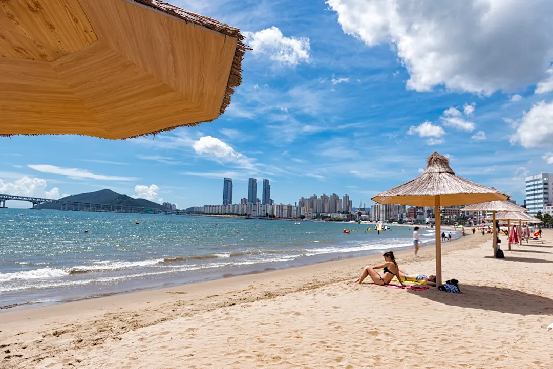 Busan Gwangalli Beach mit Wolkenhimmel und Skyline im Hintergrund.

