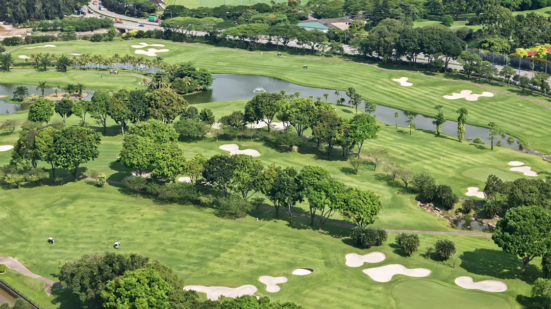  Luftaufnahme eines grünen Golfplatzes mit Sandbunkern, Teichen und umgebenden Bäumen.