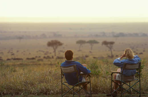 Un couple assis sur des chaises pliables observant le lever du soleil dans la savanne lors d'un voyage de noces au Kenya