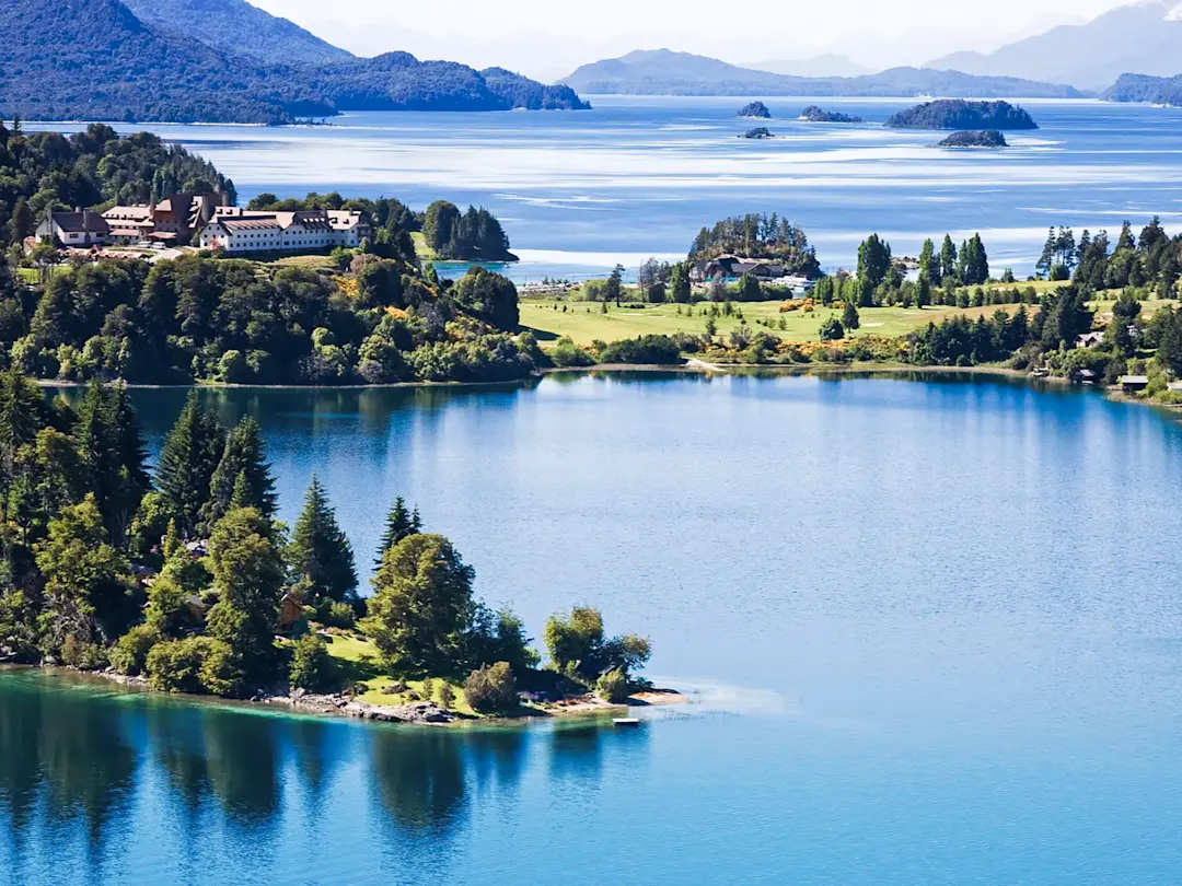 Blaues Wasser, grüne Inseln und Hotel in Berglandschaft. Bariloche, Río Negro, Argentinien.
