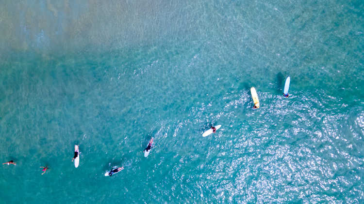 Drohnenaufnahme einer Gruppe von Surfern, die auf einem Surfbrett am Kata Beach in Phuket, Thailand, Wellen reiten. Wassersportaktivität im Sommerurlaub