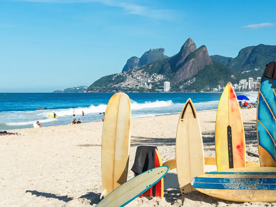 Brasilien, Rio de Janeiro, Rio de Janeiro Surfbretter im Sand mit Meer und Bergen. Rio de Janeiro, Rio de Janeiro, Brasilien.