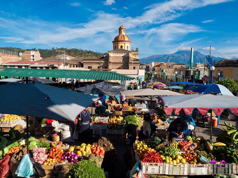 Ecuador, Imbabura, Otavalo Bunter Markt mit Obst und Gemüse vor Kirche und Bergen. Otavalo, Imbabura, Ecuador.