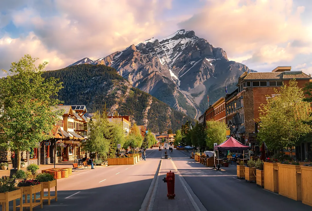 Ein farbenprächtiger Sonnenaufgangshimmel über einer Straße, die im Sommer durch die Stadt Banff führt.


