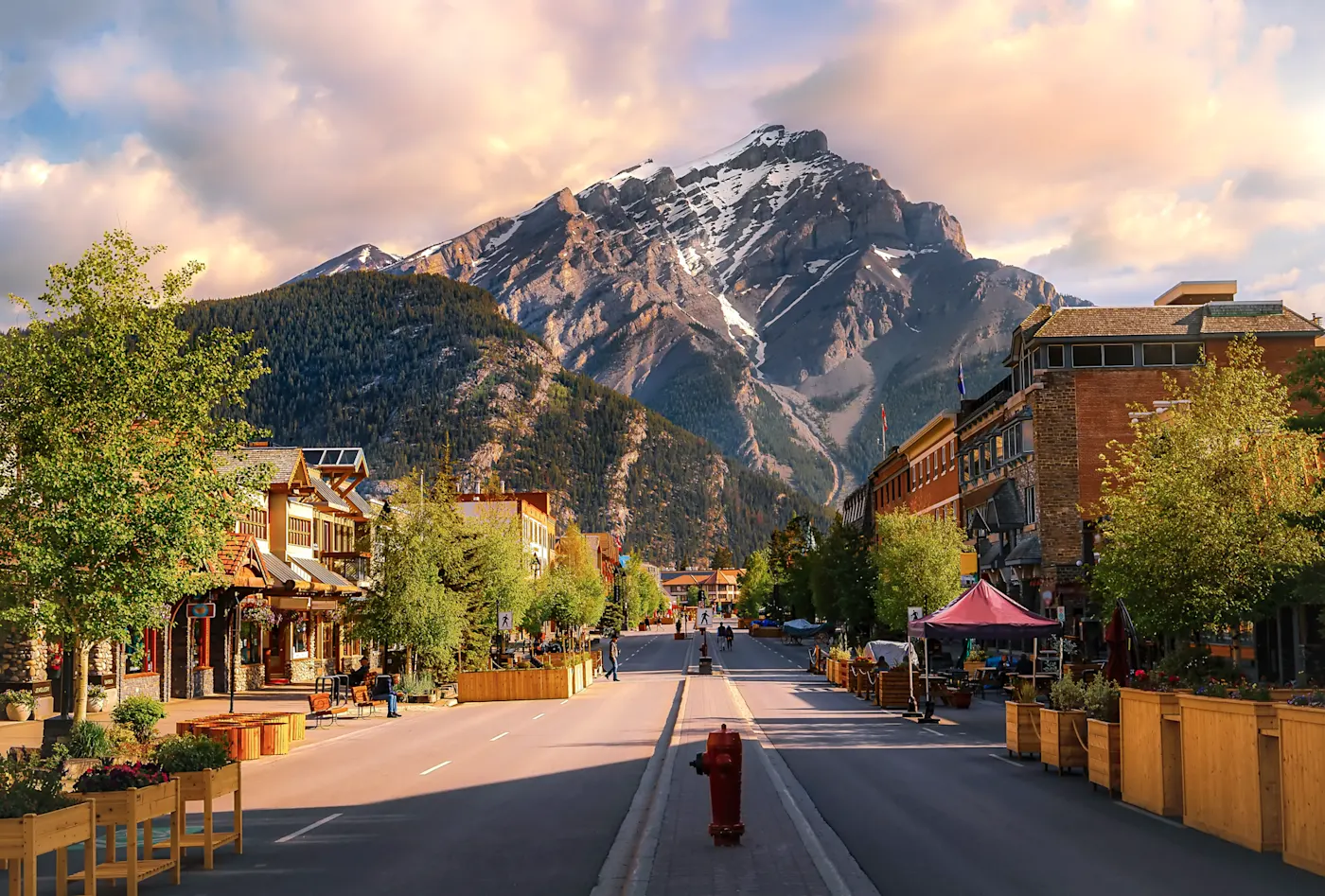 Ein farbenprächtiger Sonnenaufgangshimmel über einer Straße, die im Sommer durch die Stadt Banff führt.


