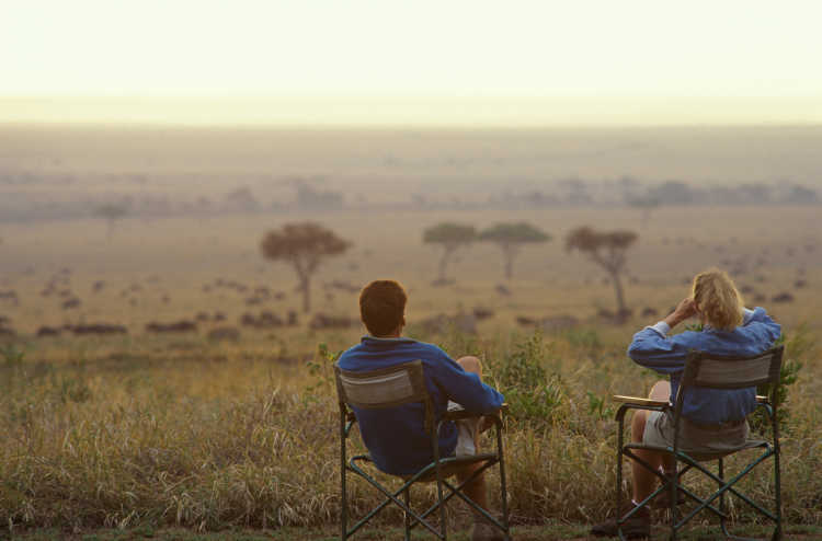 Paar sitzt auf Safari-Stühlen und blickt in die Weite der Wildnis bei einer Hochzeitsreise