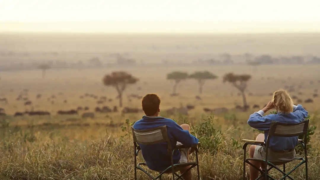Paar sitzt auf Safari-Stühlen und blickt in die Weite der Wildnis bei einer Hochzeitsreise