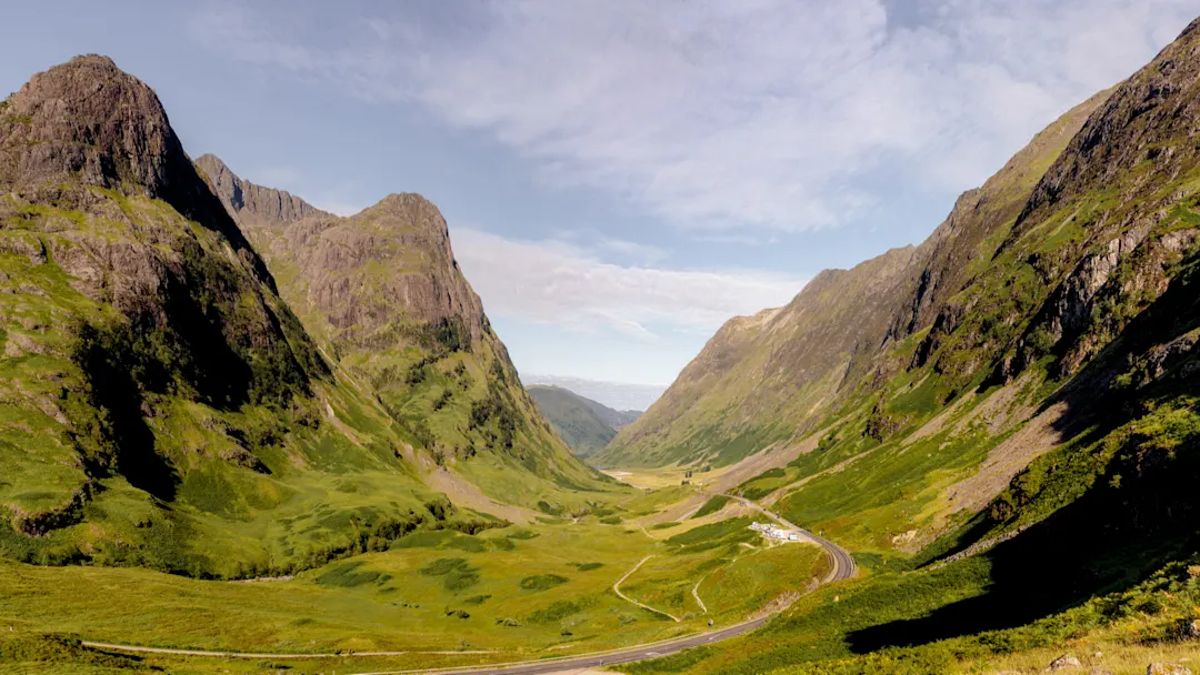 Blick auf eine schmale Talstraße im Glen Coe umgeben von grün bewachsenen Bergen