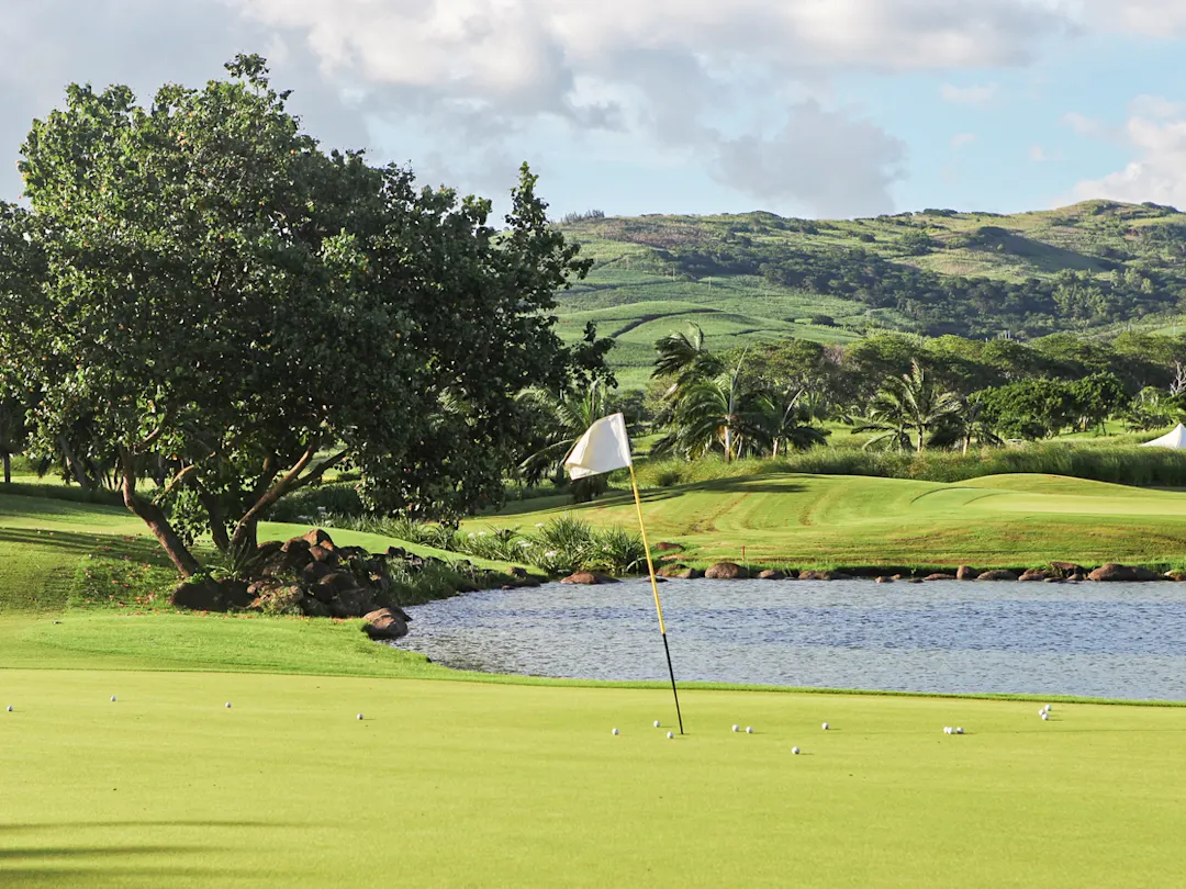 Golfplatz mit grünem Rasen, See und Hügeln im Hintergrund, umgeben von tropischer Vegetation. Mauritius.