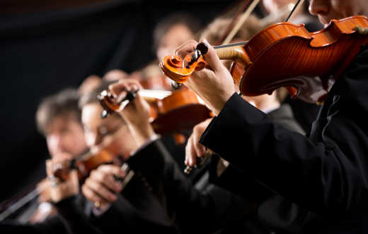 Symphonieorchester erste Violingruppe auf dunklem Hintergrund.