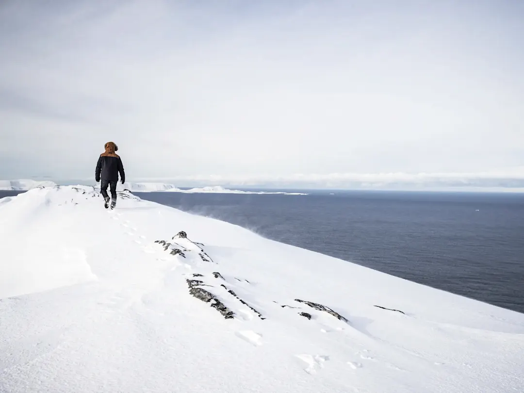 Einsamer Wanderer auf schneebedecktem Bergrücken mit Blick auf das Meer. Nordkapp, Troms og Finnmark, Norwegen.