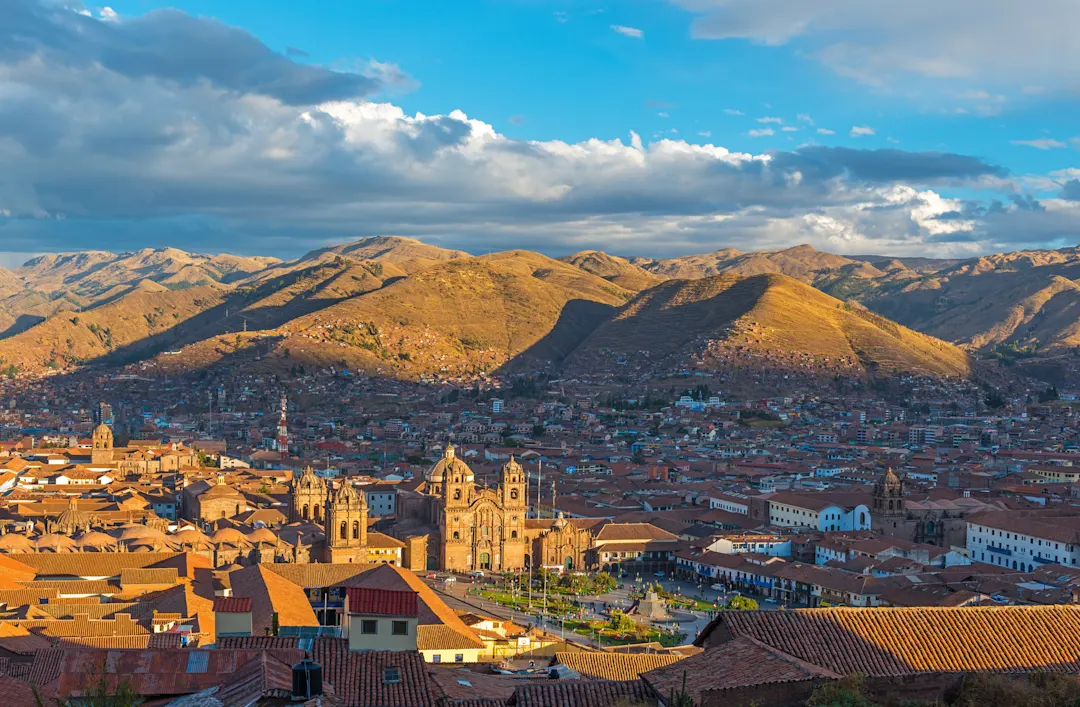 Das Stadtbild von Cusco, der alten Inka-Hauptstadt, mit den Anden im Hintergrund bei Sonnenuntergang, Peru.

