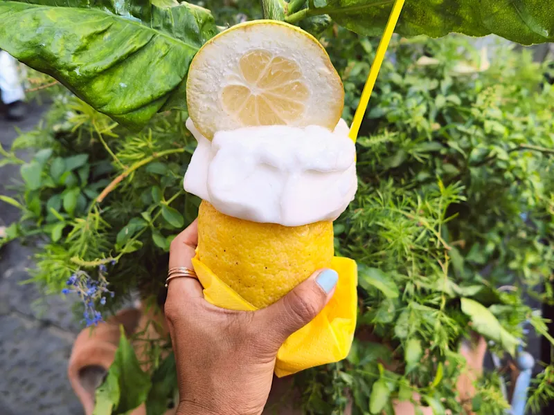 Zitronensorbet Hand hält Zitrone gefüllt mit Zitronensorbet vor einem Hintergrund von frischen Zitrusfrüchten, Italien