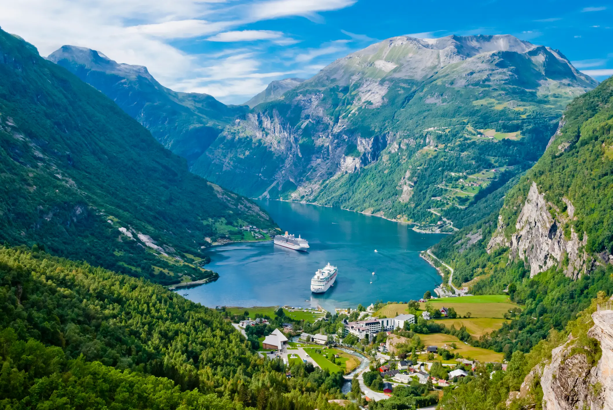 Luftaufnahme des Geirangerfjords mit saftig-grüner Sommerlandschaft und zwei Ausflusgbooten