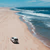 Magnifique vue aérienne sur un 4x4 en train de rouler sur une plage de sable rose pendant un voyage en Australie.