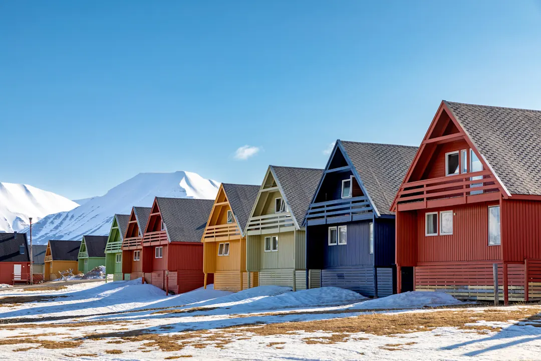 Reihe bunter Holzhäuser in Longyearbyen, Svalbard, der nördlichsten Stadt der Welt. Frühlingsszene mit Schnee auf den Bergen und im Vordergrund