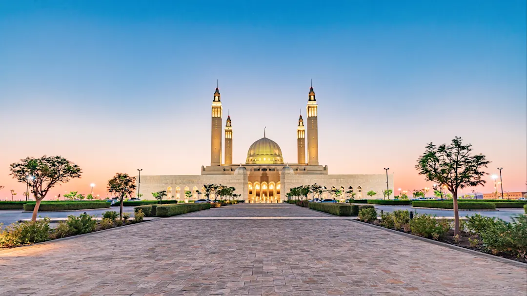 Beleuchtete Moschee im Sonnenuntergang mit weitläufigem Vorplatz. Nizwa, Ad Dakhiliyah, Oman.