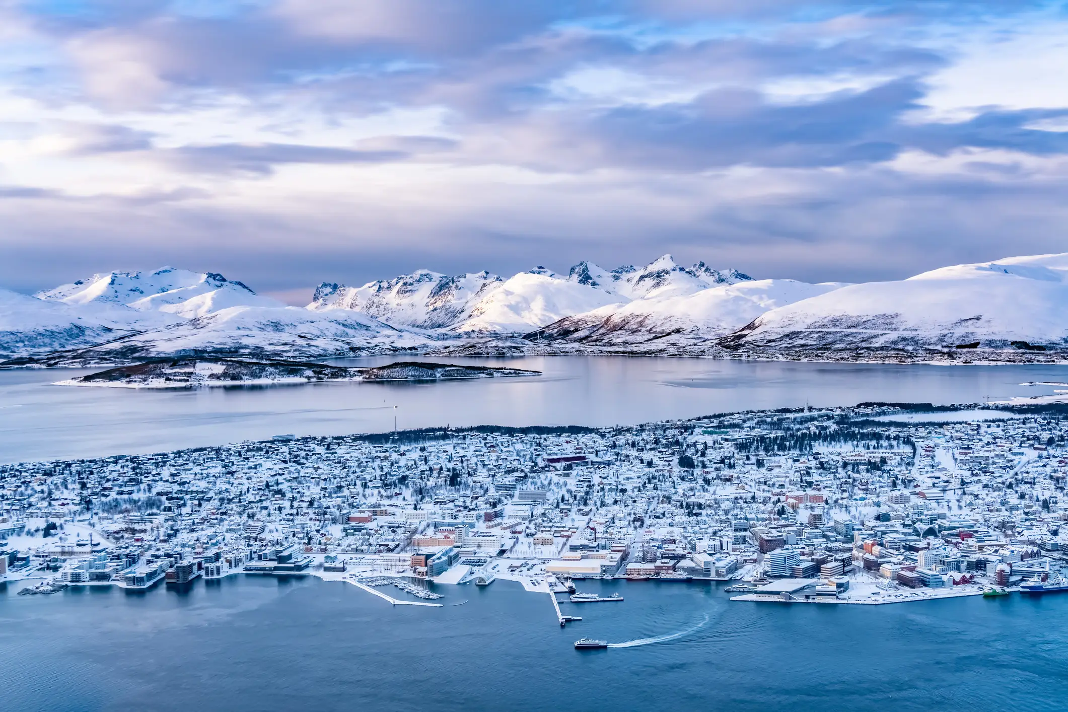 Luftaufnahme des verschneiten Tromsø an der Küste mit Bergen im Hintergrund