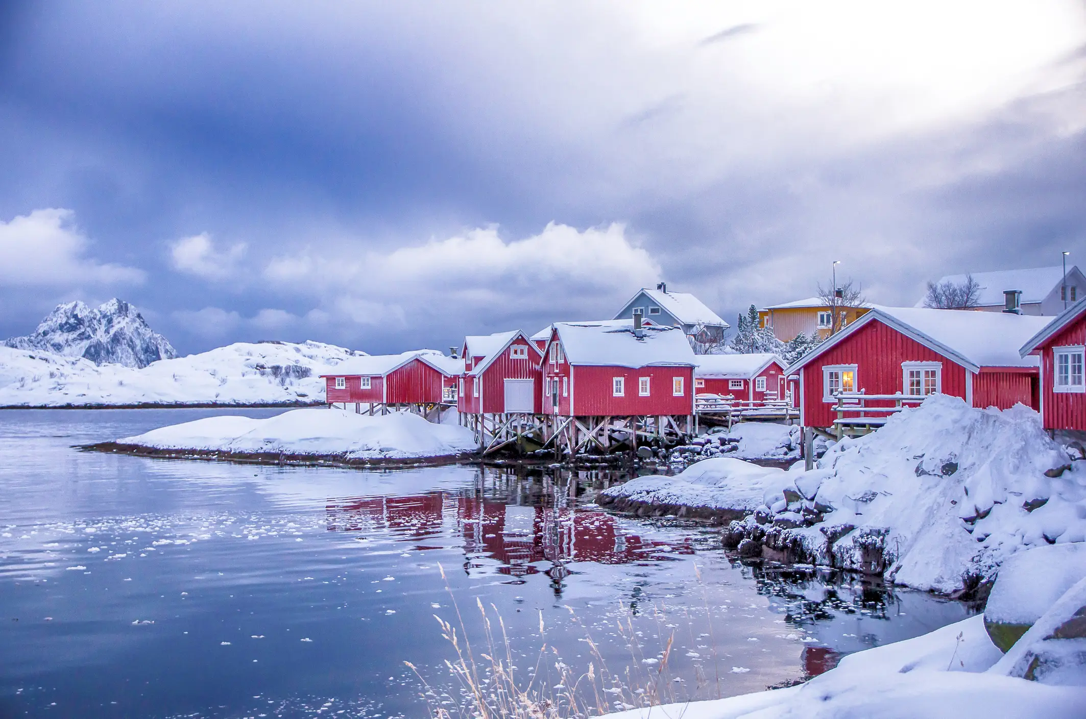 Rote Holzhäuser in einer verschneiten Landschaft am Ufer eines Fjords