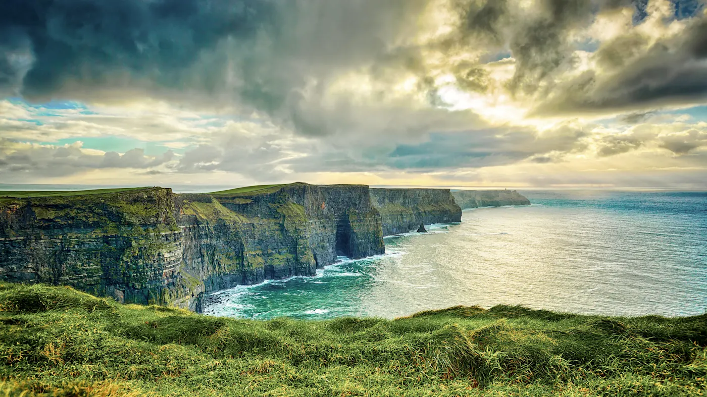 Dramatic view of the Cliffs of Moher in Ireland with dramatic cloudy sky and turquoise ocean waters below.