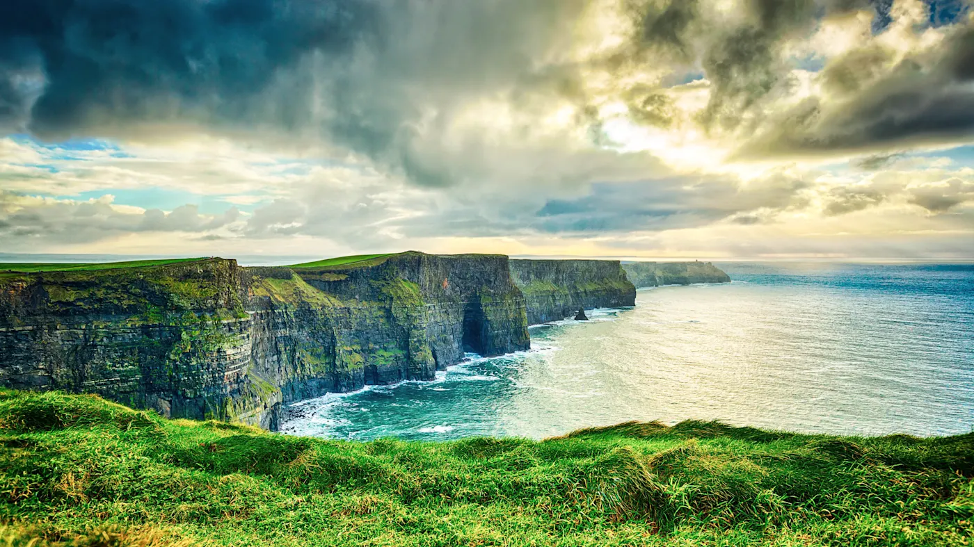 Dramatic view of the Cliffs of Moher in Ireland with dramatic cloudy sky and turquoise ocean waters below.