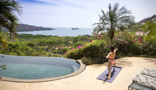 Eine Frau macht Yoga auf einer Terrasse mit Blick auf den Pazifischen Ozean in Costa Rica.

