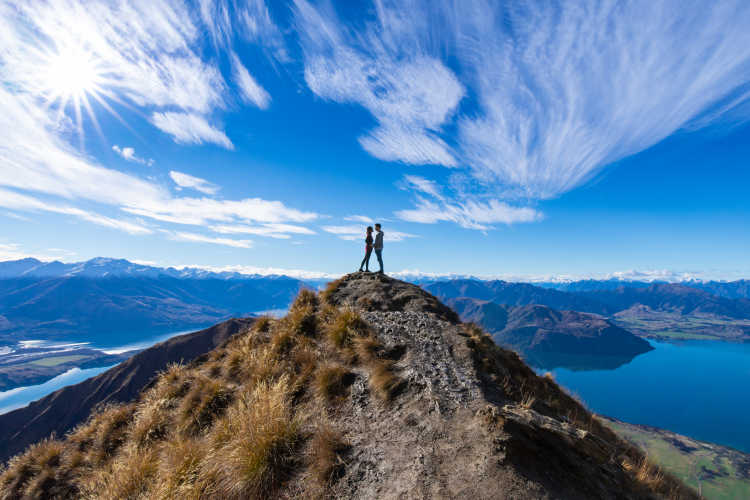 Paar küsst sich auf einem Gipfel, der einen See überragt, während einer Hochzeitsreise in Neuseeland