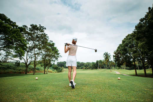 Rückansicht der asiatischen chinesischen jungen Golferin, die ab- und schwingt ihren Fahrerclub auf dem Golfplatz